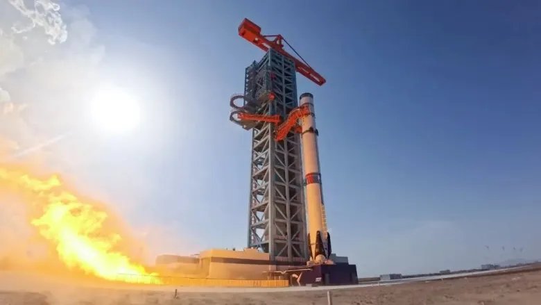 a white rocket conducts an engine test on a launch pad beneath a blue sky