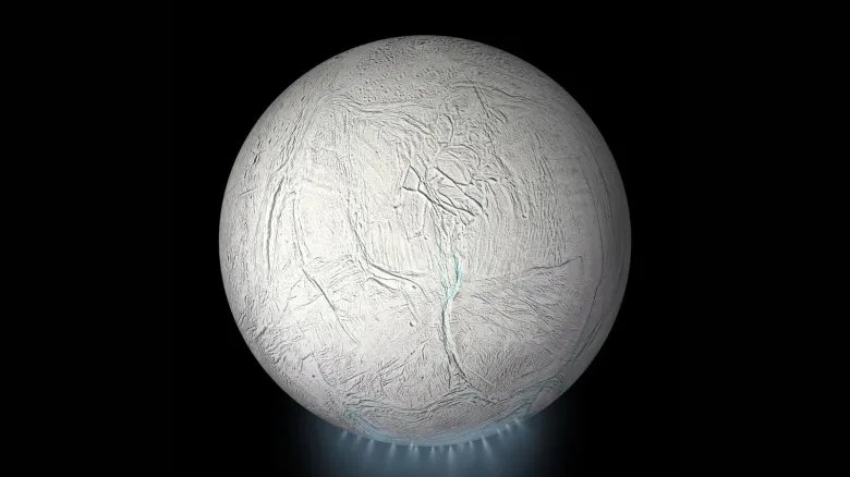 A photo of the moon Enceladus with a blue plume of steam underneath it as it sits in the darkness of space